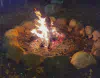 A campfire burning at night in a circular rock firepit.